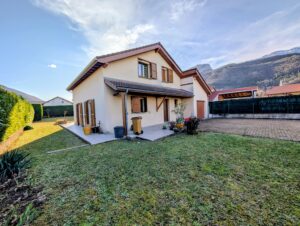 Maison individuelle avec jardin et terrasse, au pied d’un massif montagneux.