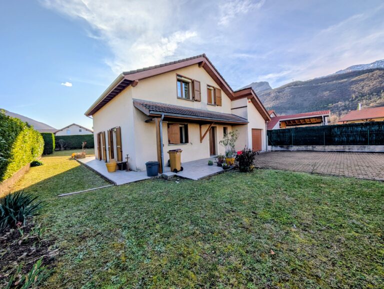 Maison individuelle avec jardin et terrasse, au pied d’un massif montagneux.